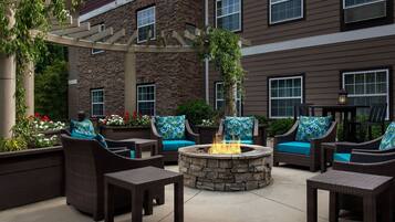 An outdoor patio area with wicker furniture, a stone fire pit, and a pergola.