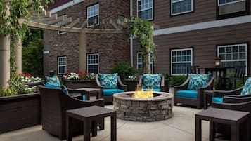 An outdoor patio area with wicker furniture, a stone fire pit, and a pergola.