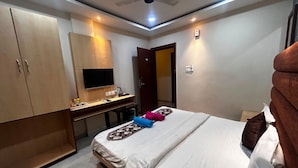 Een hotelkamer met een bed, een bureau met een flatscreen televisie, een plafondventilator en een deur naar een andere kamer.