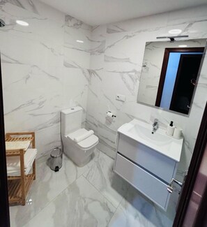 A bathroom with a marble wall, a toilet, a sink, and a mirror. - Apartamento Barbanzaarousa (Boiro)
