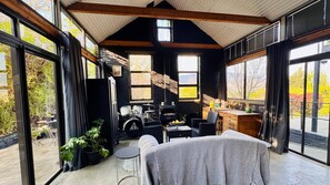 A cozy interior with a stone fireplace, wooden beams, and large windows offering a view of the outdoors.