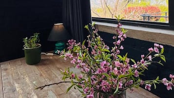 A room with a large window, a wooden table, a potted plant, and a vase with flowers.