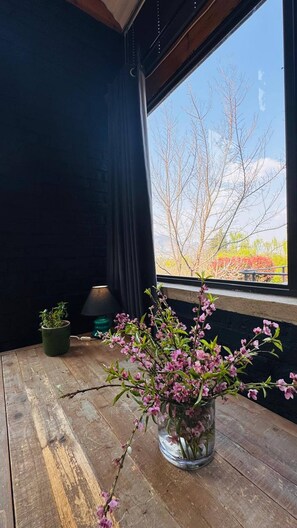 Una habitación con un ventanal grande, una mesa de madera, una planta en maceta y un florero con flores.