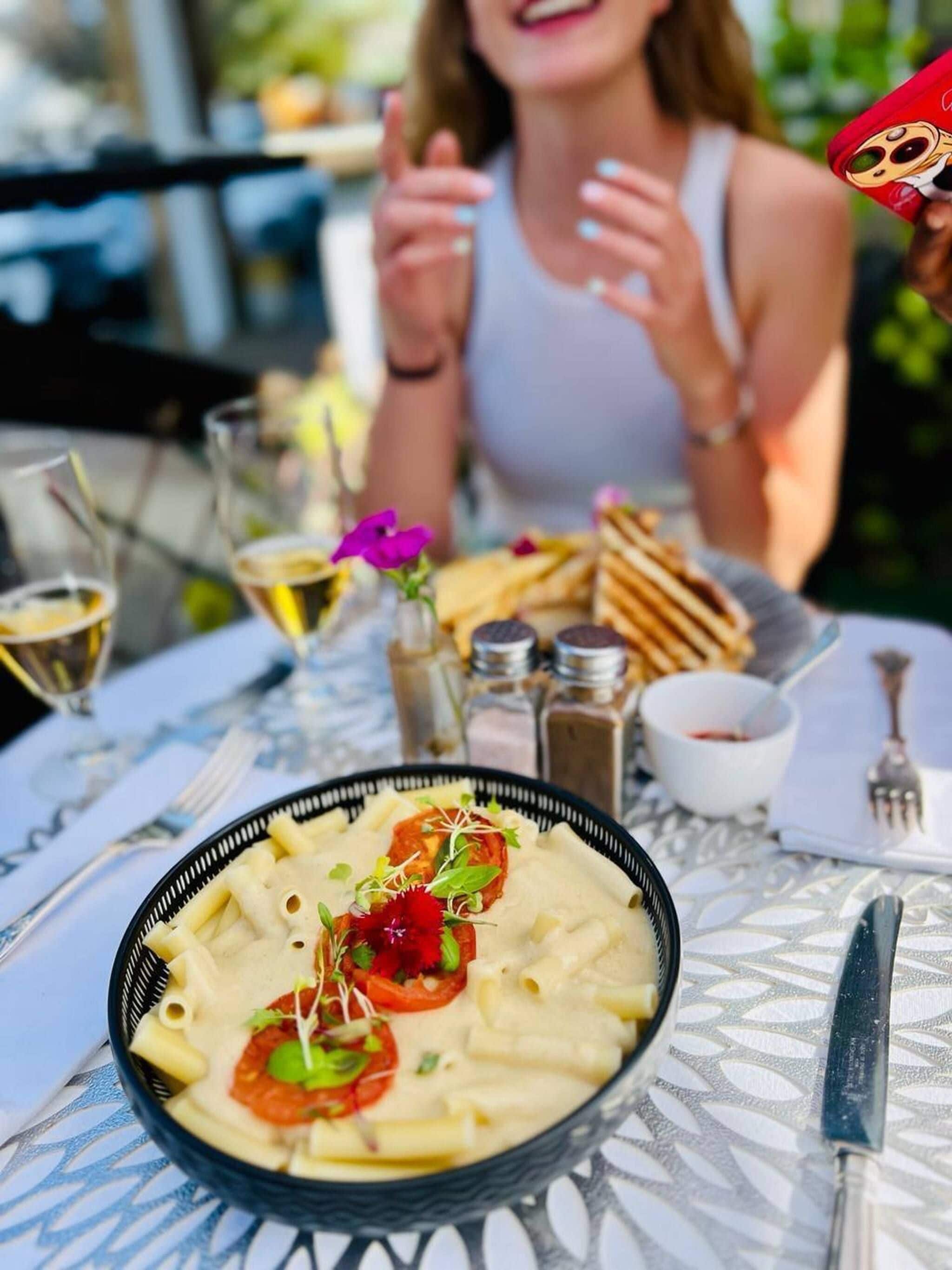A dining table with a plate of pasta, a glass of wine, and a dessert cup.