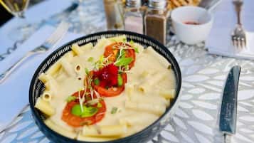 A dining table with a plate of pasta, a glass of wine, and a dessert cup.