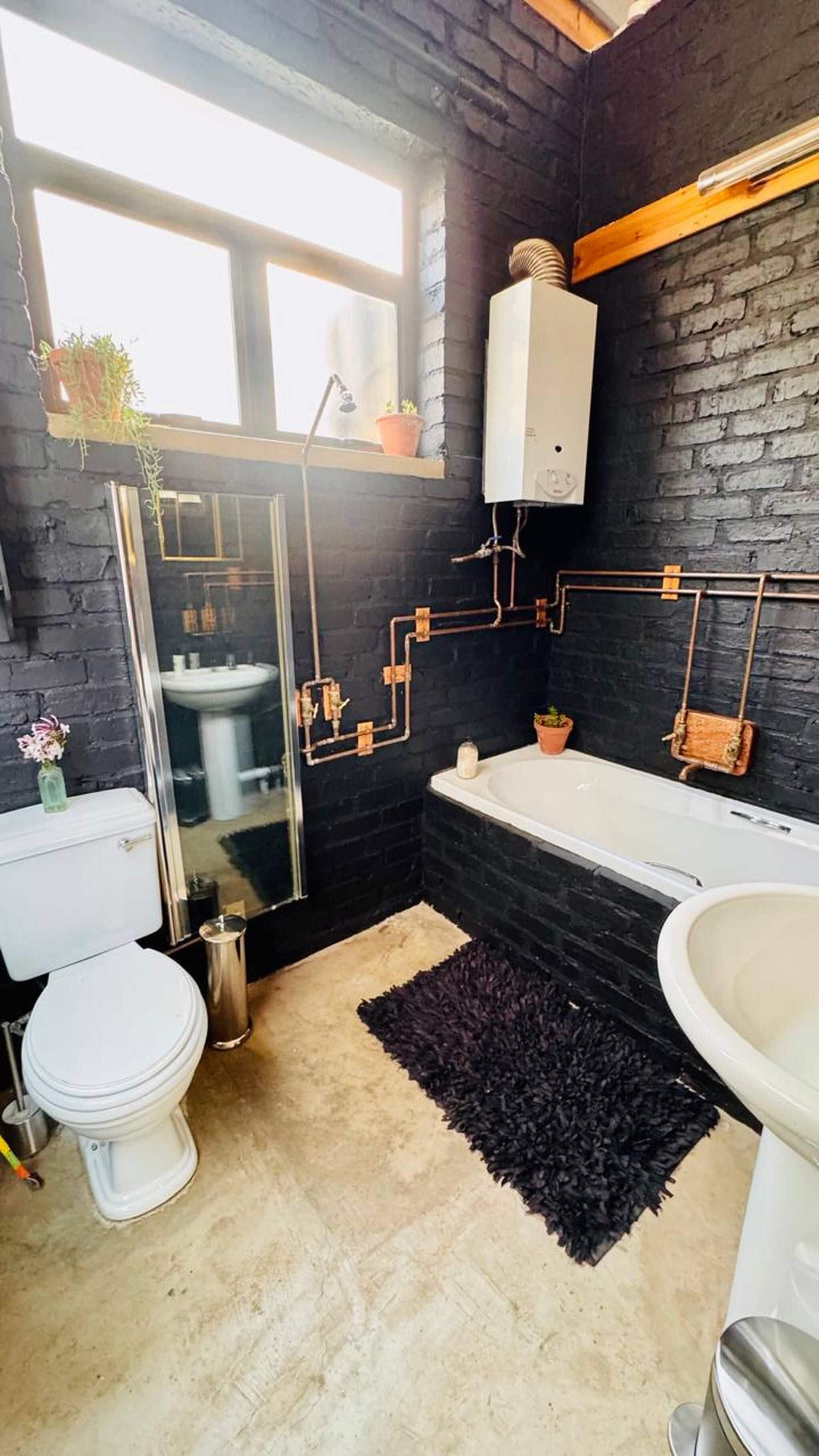 A modern bathroom with a black brick wall, a white toilet, a bathtub, and a sink.
