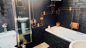 A modern bathroom with a black brick wall, a white toilet, a bathtub, and a sink.