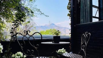 A patio with two metal chairs and a table, surrounded by greenery and a view of mountains.