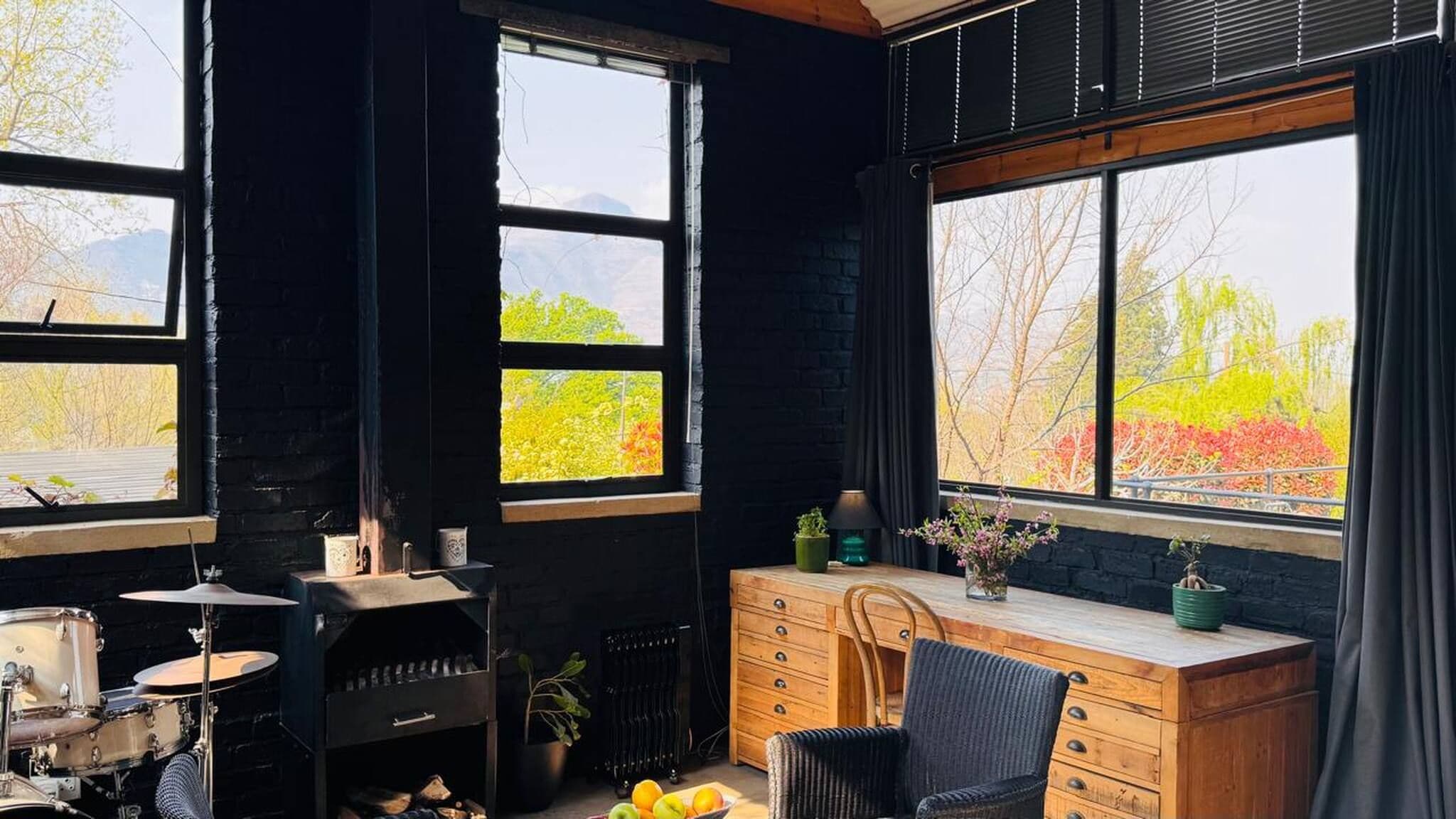 A room with a drum set, a radiator, a wooden desk, and a chair.