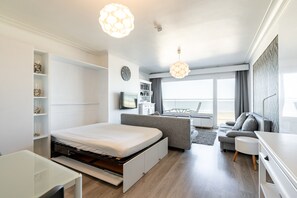 A modern hotel room with a bed, a desk, a sofa, a TV, and a balcony with a view. - Studio by the Sea With Stunning Terraces (Blankenberge)