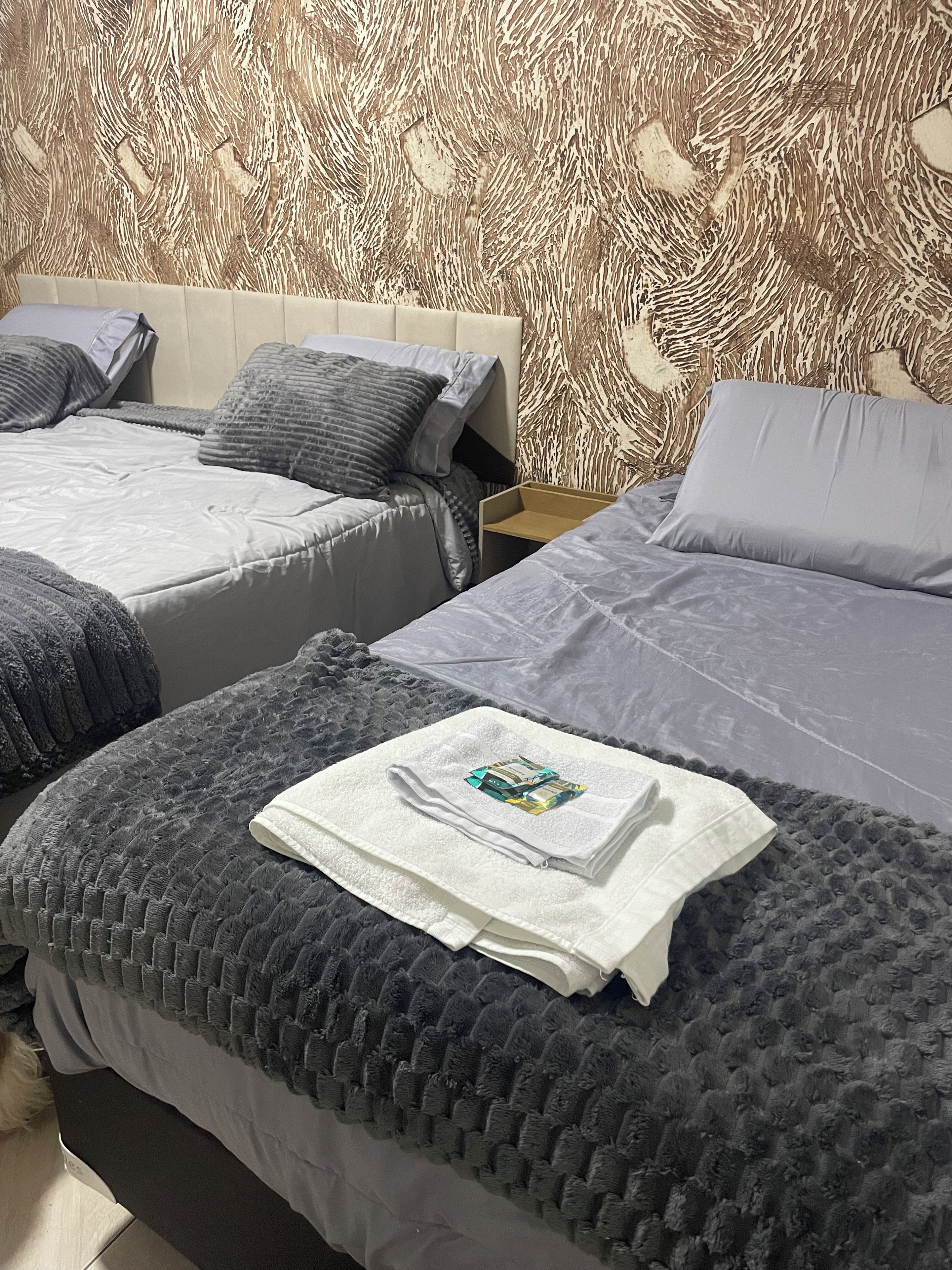 A hotel room with two beds, a wooden headboard, and a patterned wallpaper.