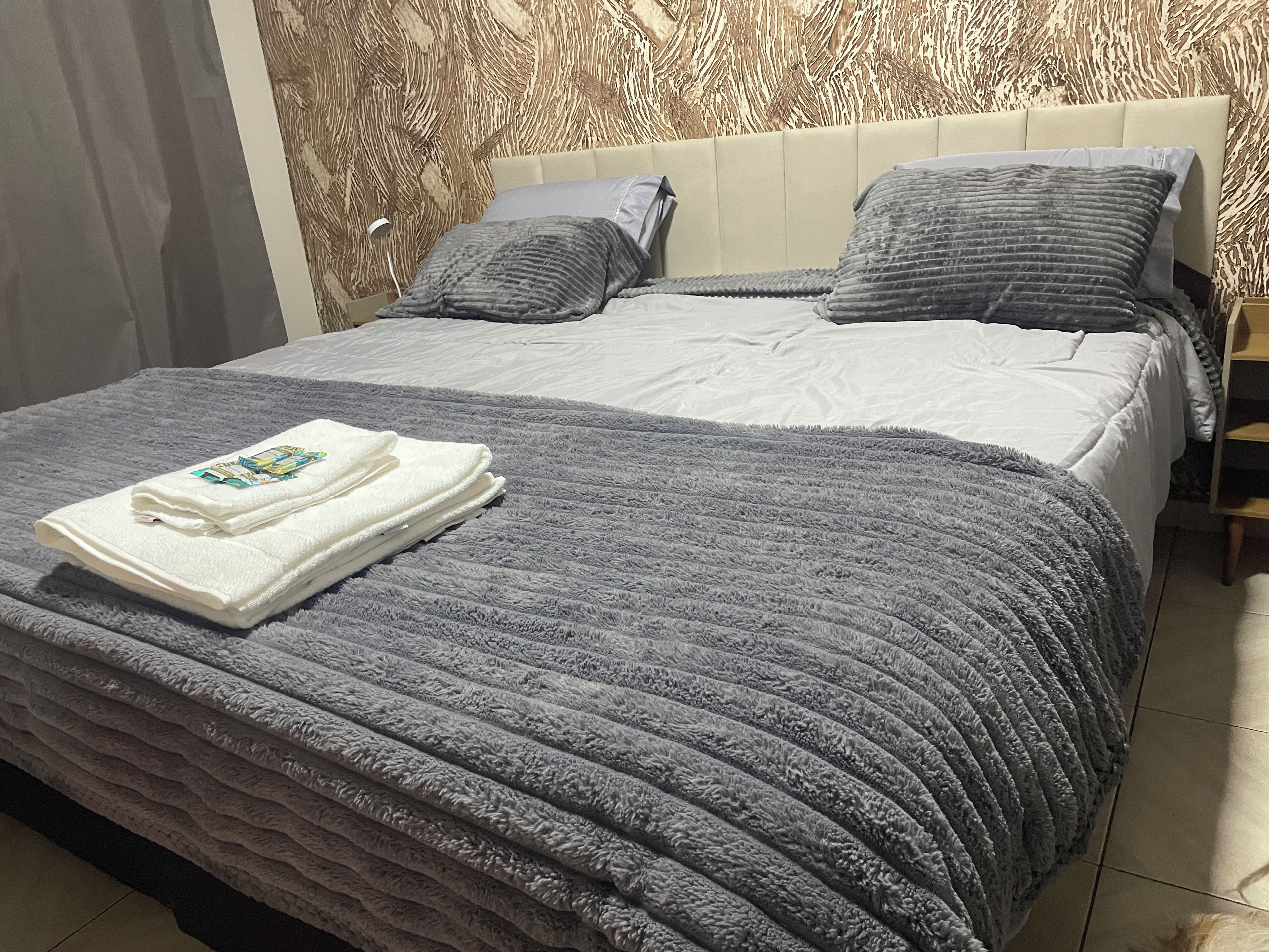 A neatly made bed with a grey blanket and a folded white towel.