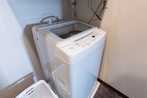 A front-loading washing machine with a control panel, a power cord, and a wall outlet. - Villa Arco Miyakojima (Miyakojima City)