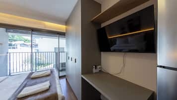 Et moderne hotelværelse med balkon, et fladskærms-tv ophængt på væggen og en træbænk med håndklæder.