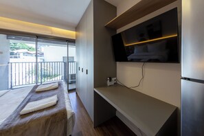 A modern hotel room with a balcony, a flat-screen TV mounted on the wall, and a wooden bench with towels. - Palhetas by Bhomy (São Paulo)