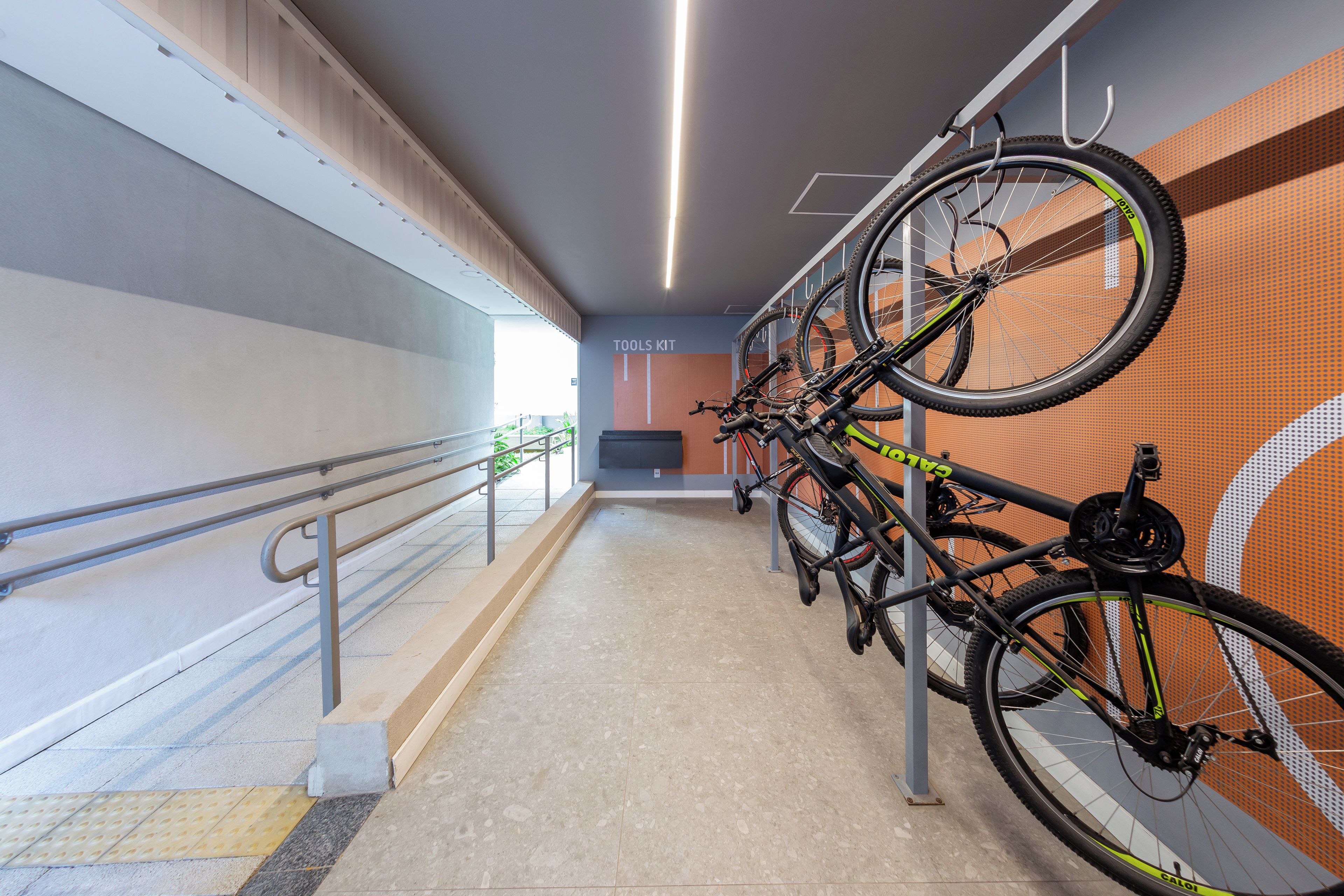 Un support à vélos avec plusieurs vélos, une pancarte indiquant « OUTILS », et un sol carrelé avec une main courante.