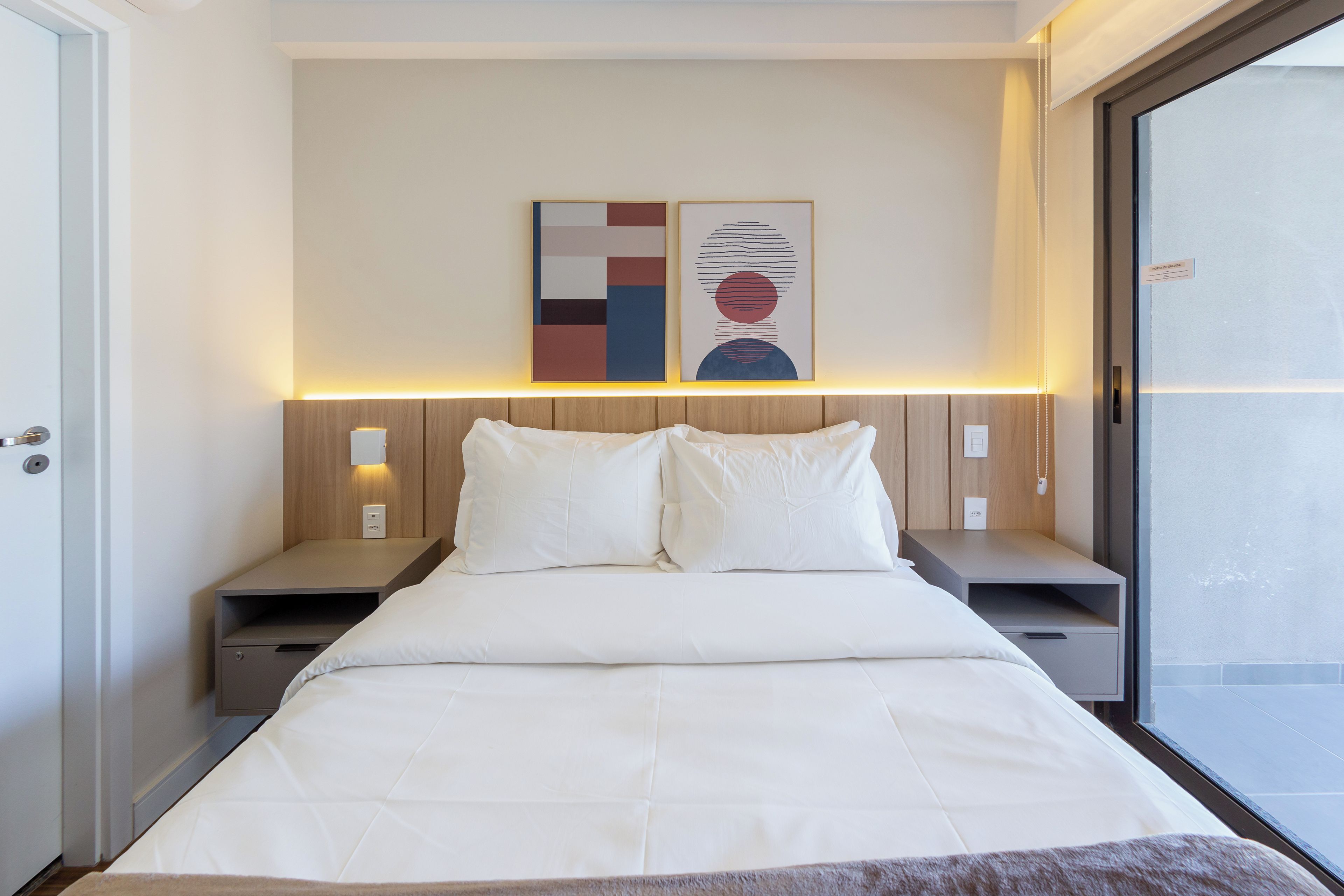 Une chambre d’hôtel comprenant un lit, des tables de chevet, une petite table, une lampe fixée au mur et une fenêtre.