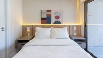 Une chambre d’hôtel comprenant un lit, des tables de chevet, une petite table, une lampe fixée au mur et une fenêtre.