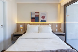 A hotel room with a bed, bedside tables, a nightstand, a wall-mounted light, and a window. - Palhetas by Bhomy (São Paulo)