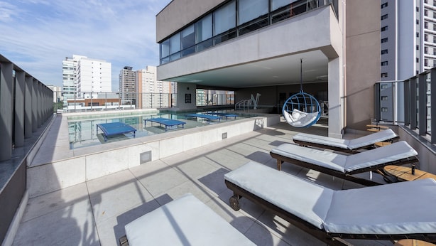 Un área de piscina en la azotea con sillones de descanso, una hamaca colgante y vistas de edificios circundantes.