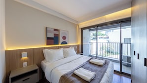 Una habitación de hotel con cama, mesitas de noche, una obra de arte colgada en la pared y un balcón con vistas.