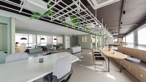 Un espacio de oficina moderno con una larga mesa, sillas y un alto techo con plantas.