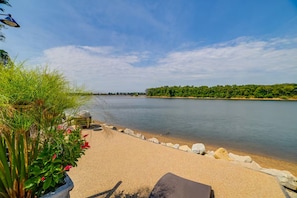A beach with a clear view of the water, a sandy area with rocks, and some greenery. - Riverfront Living (Clifton)