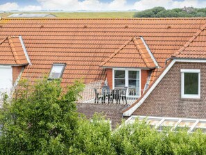 Ein Wohngebäude mit rotem Ziegeldach, einer Ziegel-Fassade und einem kleinen Balkon mit Metallgeländer.