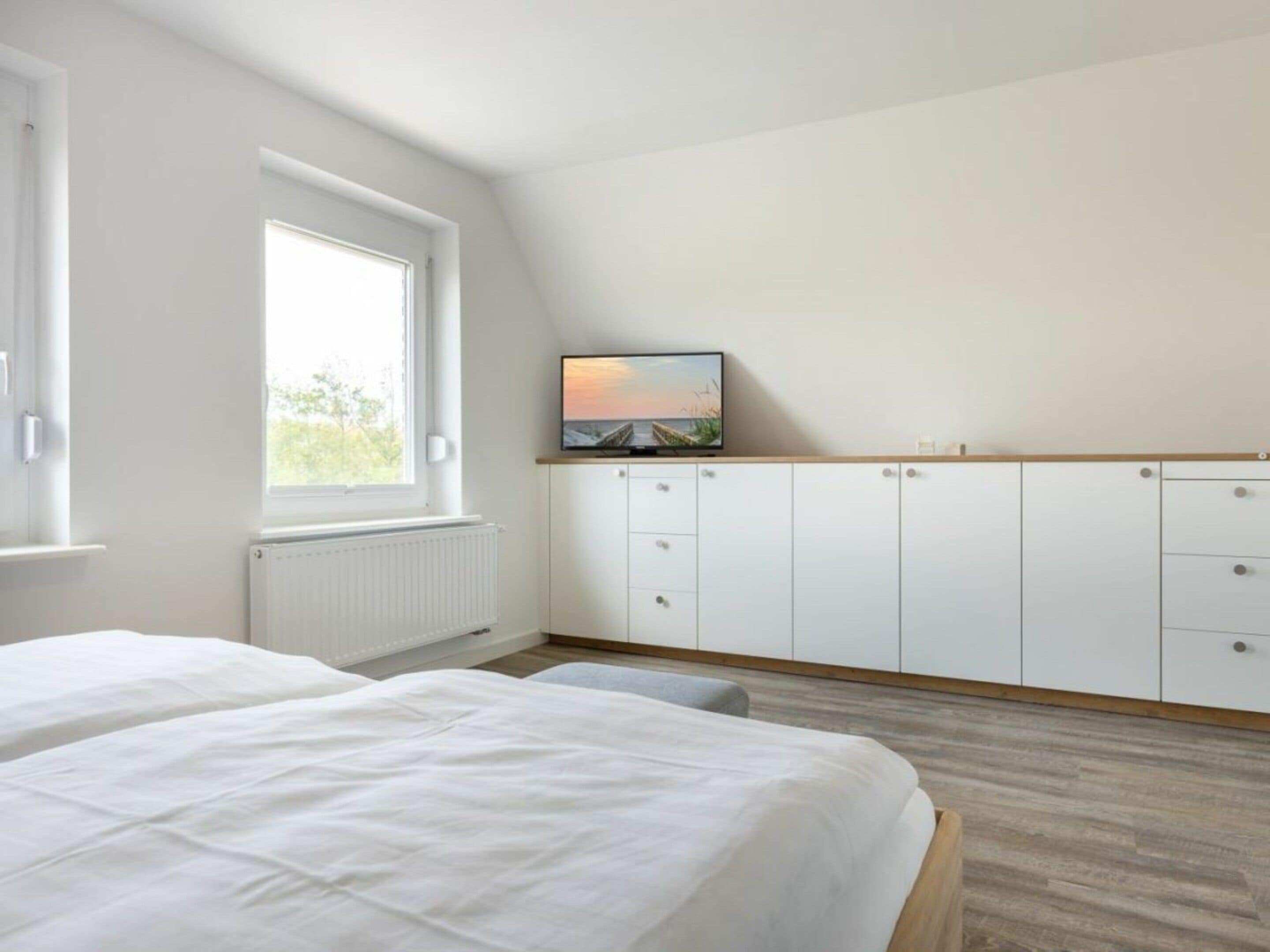 Quarto com cama, televisão em prateleira, janela e radiador.