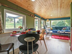 A dining area with a table set for two, a chair, and a view of the outdoors through large windows. - Orchard Lodge (Dover)