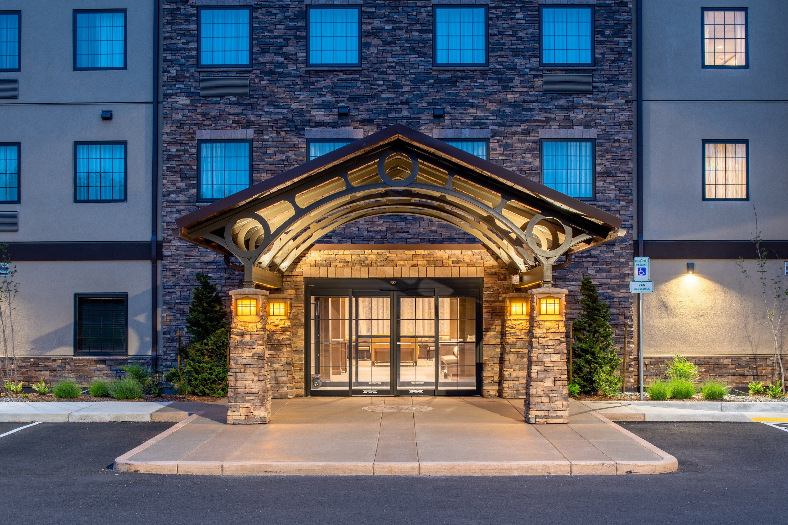 A building entrance with a stone archway, large glass doors, and a parking sign.