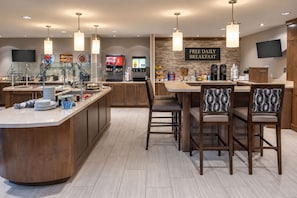 A modern kitchen with a breakfast bar, a Coca-Cola dispenser, and a sign offering free daily breakfast.
