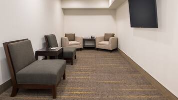 A hotel room with a carpeted floor, two armchairs, a sofa, a small table, and a flat-screen TV mounted on the wall.