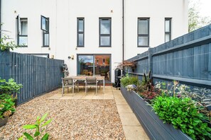 Un edificio residencial moderno con un patio, una mesa y sillas, y varias plantas.