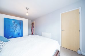 Un dormitorio con cama, un radiador, una puerta y un cuadro en la pared.