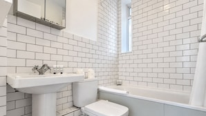 Un baño con paredes de azulejos blancos, un lavamanos, un inodoro y una bañera.