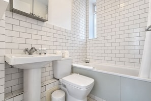 Ein Badezimmer mit weißen Fliesen, einem Waschbecken, einer Toilette und einer Badewanne.