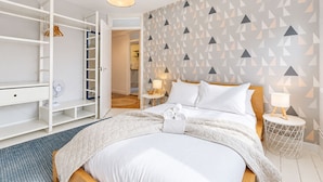 Una habitación de hotel con cama, mesitas de noche, un armario y una pared con estampado geométrico.