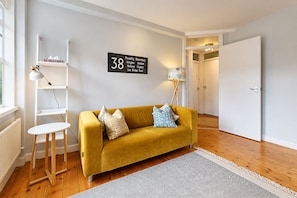 Ein Zimmer mit einem senfgelben Sofa, einem weißen Beistelltisch, einer Stehlampe, einem weißen Heizkörper und einem Schild mit der Nummer 38.