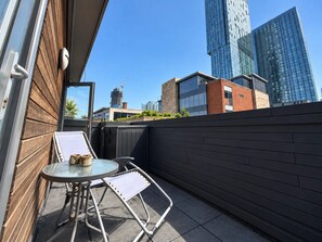 Ein Balkon mit Glastisch und Stühlen, einer Holzwand und Blick auf moderne Gebäude.