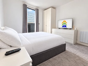 Ein Hotelzimmer mit einem Bett, einem Fernseher, einer Fernbedienung, einem Kleiderschrank und einem Fenster mit Vorhängen.