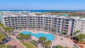 A multi-story hotel with a central swimming pool surrounded by palm trees and a beach area. - Gulf View Corner Condo + Lazy River + Beach Chairs (Fort Walton Beach)