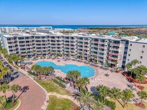 A multi-story hotel with a central swimming pool surrounded by palm trees and a beach area. - Gulf View Corner Condo + Lazy River + Beach Chairs (Fort Walton Beach)