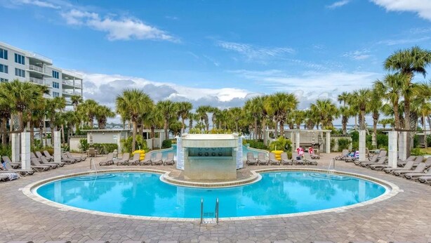 A swimming pool with lounge chairs and palm trees. - Gulf View Corner Condo + Lazy River + Beach Chairs (Fort Walton Beach)