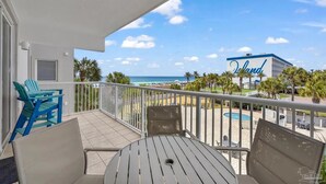 A balcony with a view of the beach, a pool, and a building with 'Island' written on it. - Gulf View Corner Condo + Lazy River + Beach Chairs (Fort Walton Beach)