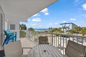 A balcony with a view of the beach, a pool, and a building with 'Island' written on it. - Gulf View Corner Condo + Lazy River + Beach Chairs (Fort Walton Beach)