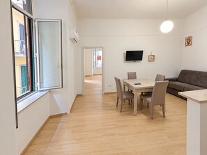 A modern living room with a dining area, a flat-screen TV mounted on the wall, and a window with a view of the outside. - Pinuccia and Totore Sweet Home (Napoli)