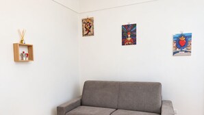 A neutral-colored room with a grey sofa, a wooden shelf with a spray bottle, and three artworks on the wall. - Vrbo Property (Napoli)