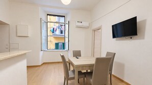 A room with a dining table, chairs, a TV mounted on the wall, and an air conditioning unit. - Vrbo Property (Napoli)