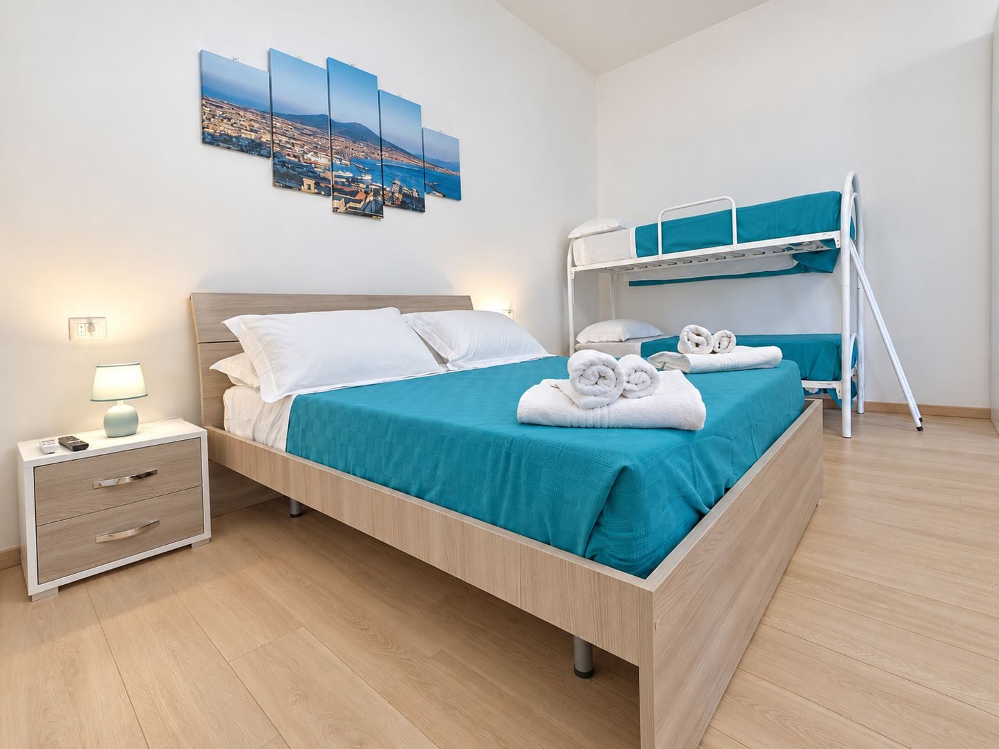 Une chambre d’hôtel comprenant un lit, une table de chevet avec une lampe, un lit superposé et une œuvre d’art accrochée au mur.